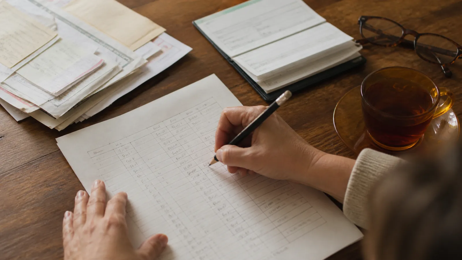 Hand-drawn senior care budget worksheet being filled in beside bills and a checkbook